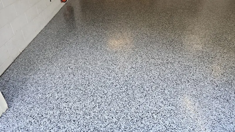 Finished gray and black polyaspartic flake floor with coated cove base in a clean garage