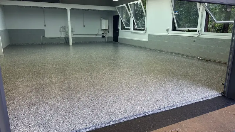Gray and white polyaspartic flake floor filling a clean, empty garage with block walls and windows