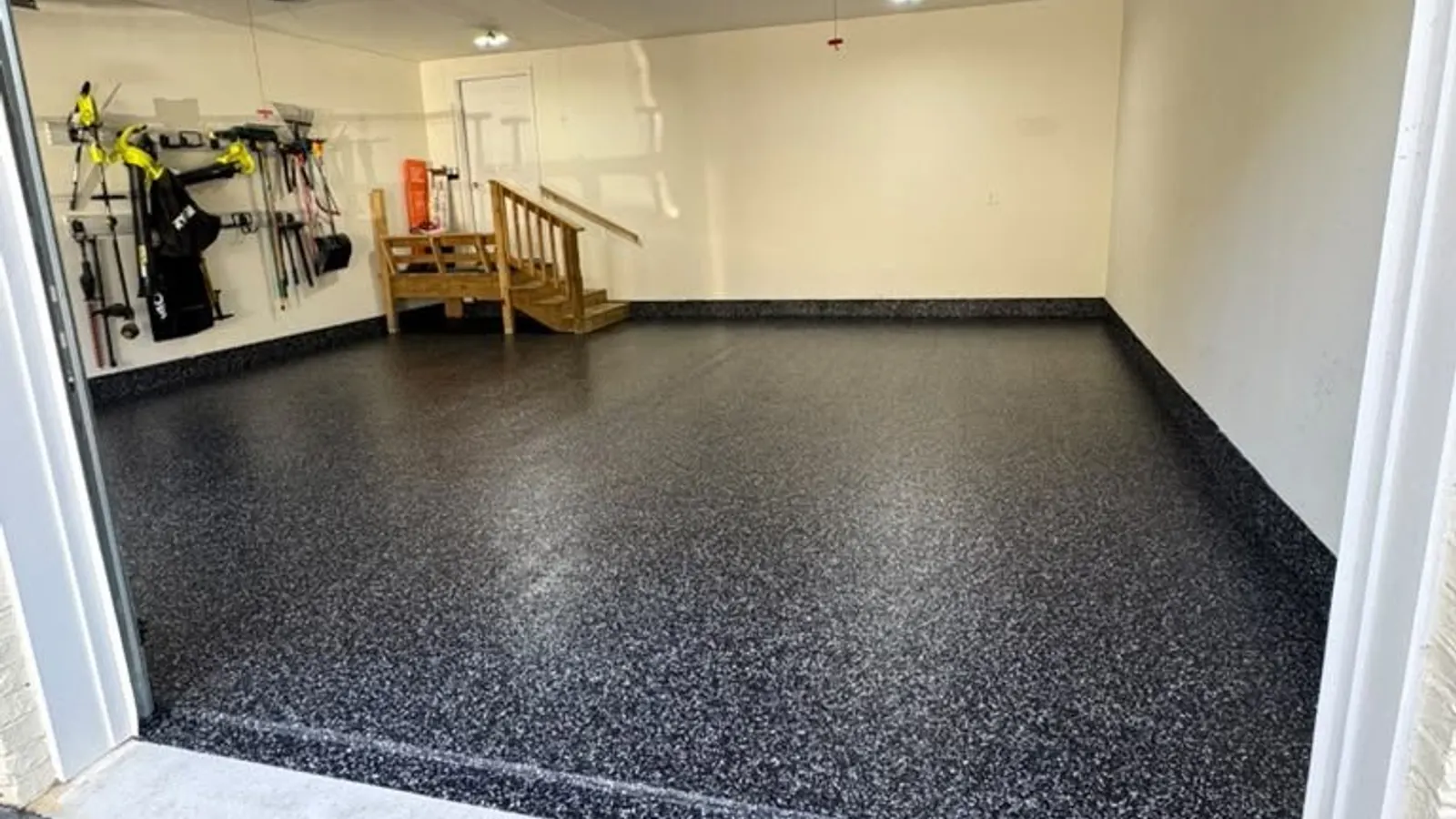 Finished black and white polyaspartic flake garage floor with coved edges in a clean, empty two-car garage