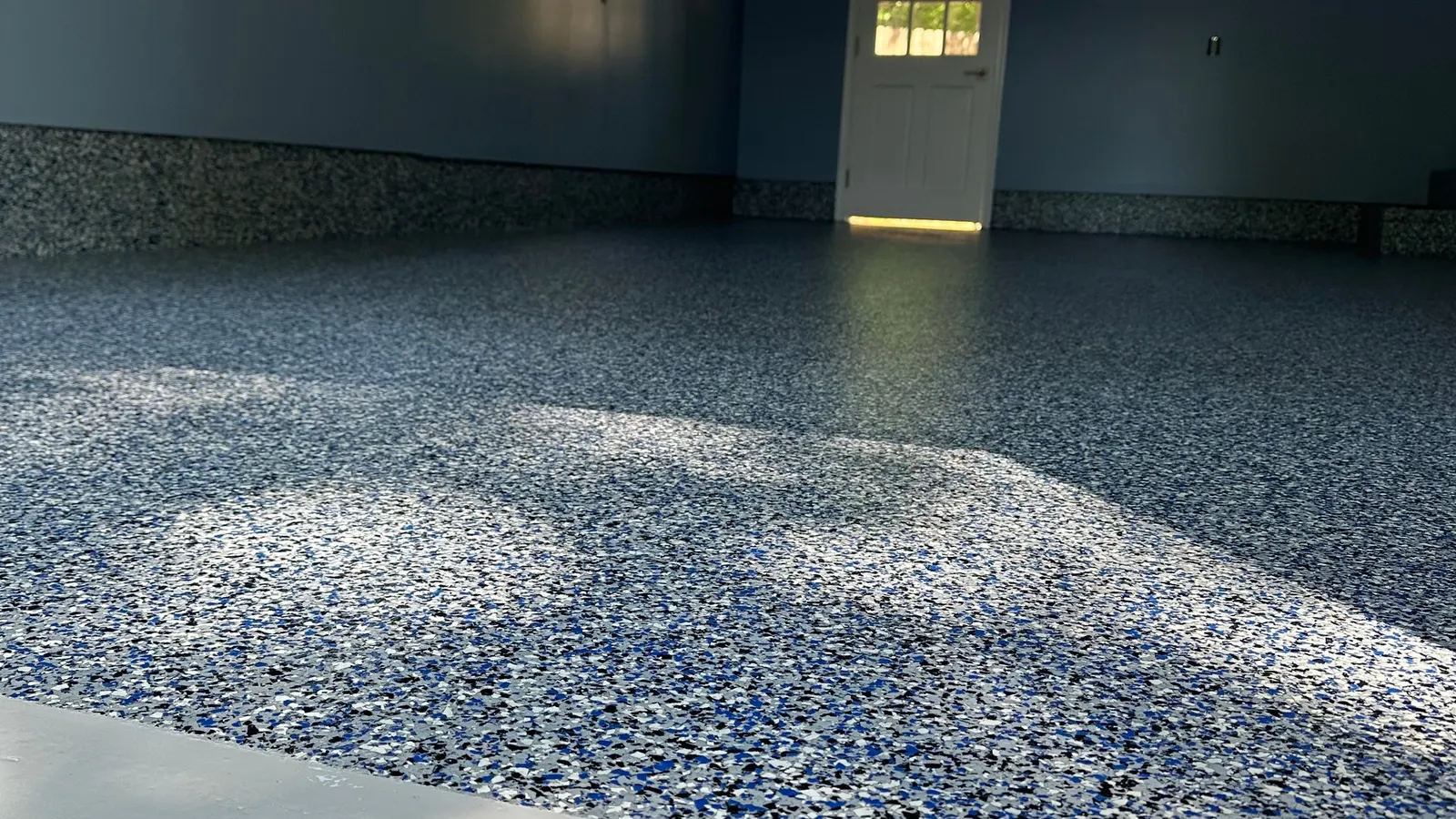 Blue, white and black polyaspartic flake garage floor with coved base, finished and glossy near a white door