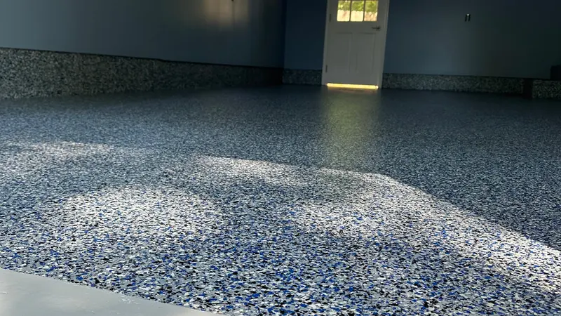 Blue, white and black polyaspartic flake garage floor with coved base, finished and glossy near a white door