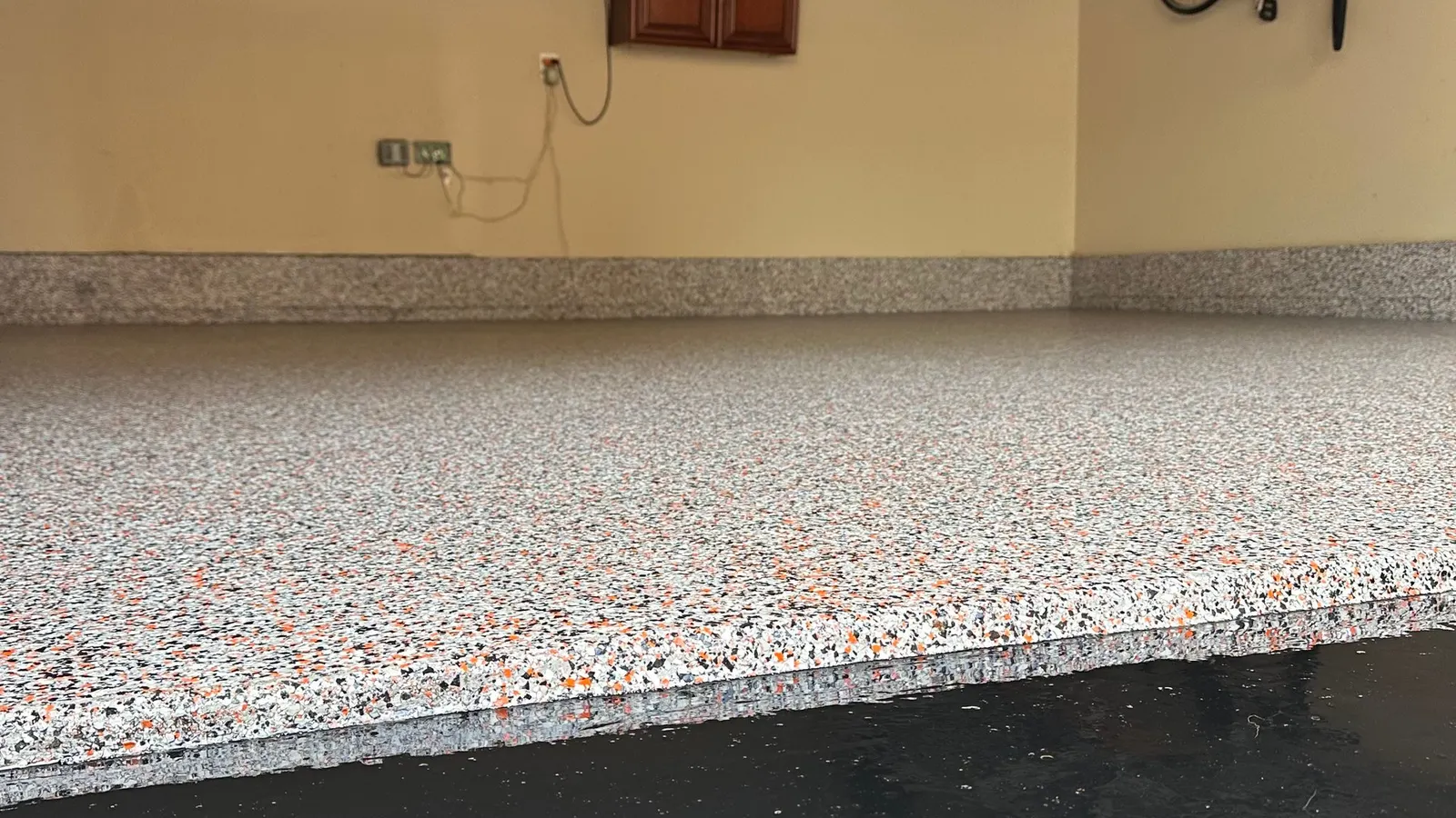 Gray and orange polyaspartic flake garage floor with matching flake cove base, finished wall to wall.