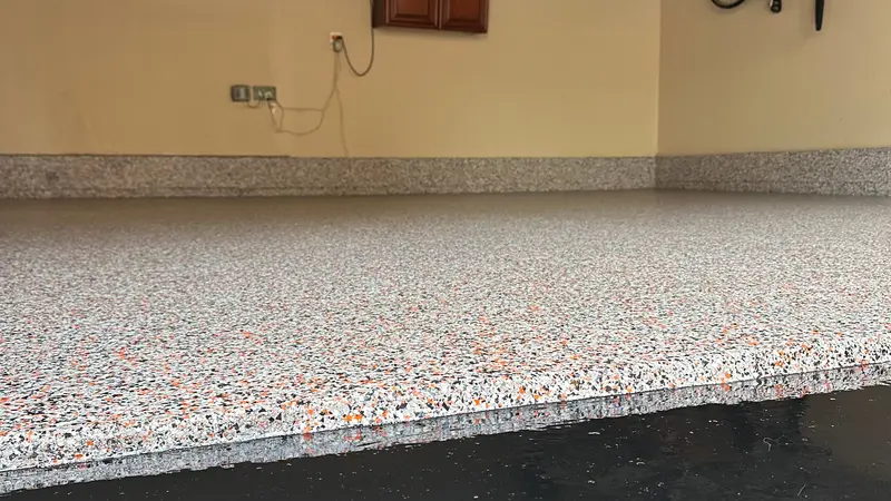 Gray and orange polyaspartic flake garage floor with matching flake cove base, finished wall to wall.
